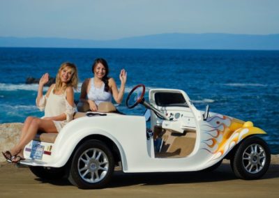 Two Women Sitting in a Roadster With Ocean and Mountain Views