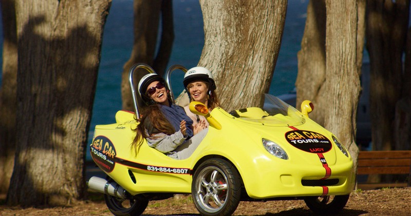 Two Women with Smiling Faces Driving Past Large Trees in a GoCar