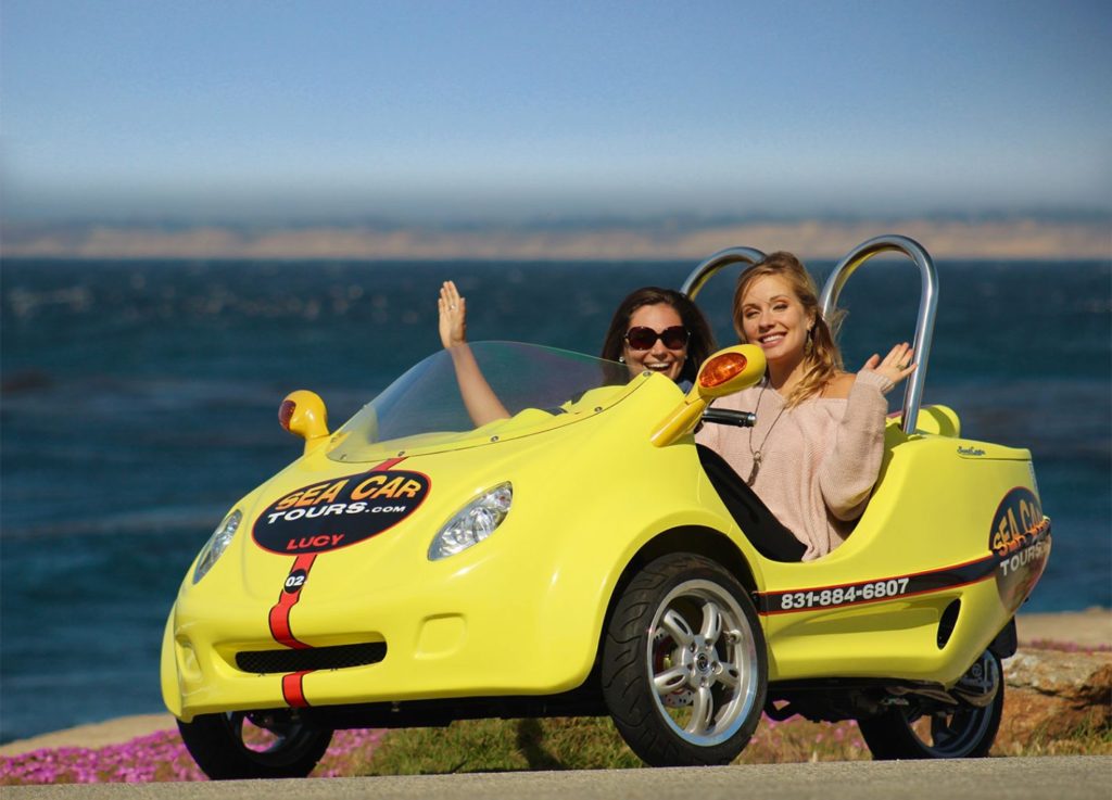 Two Ladies Sitting in a Go Car in Front of the Ocean Smiling and Waving