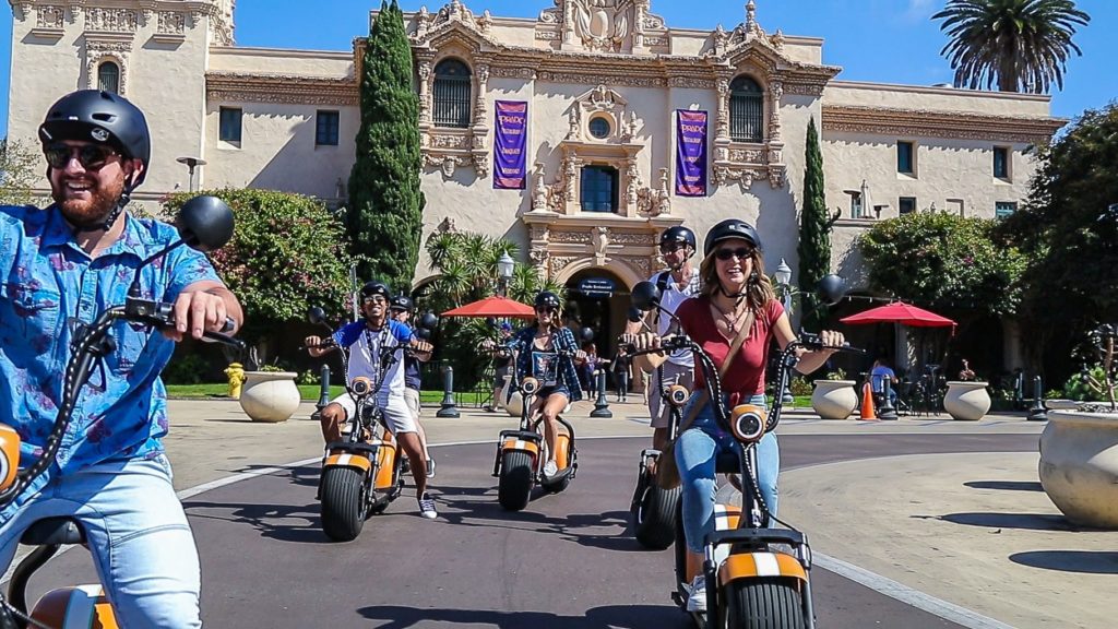 Several Fat Tire Scooter Passengers In Front of Historic San Diego Building