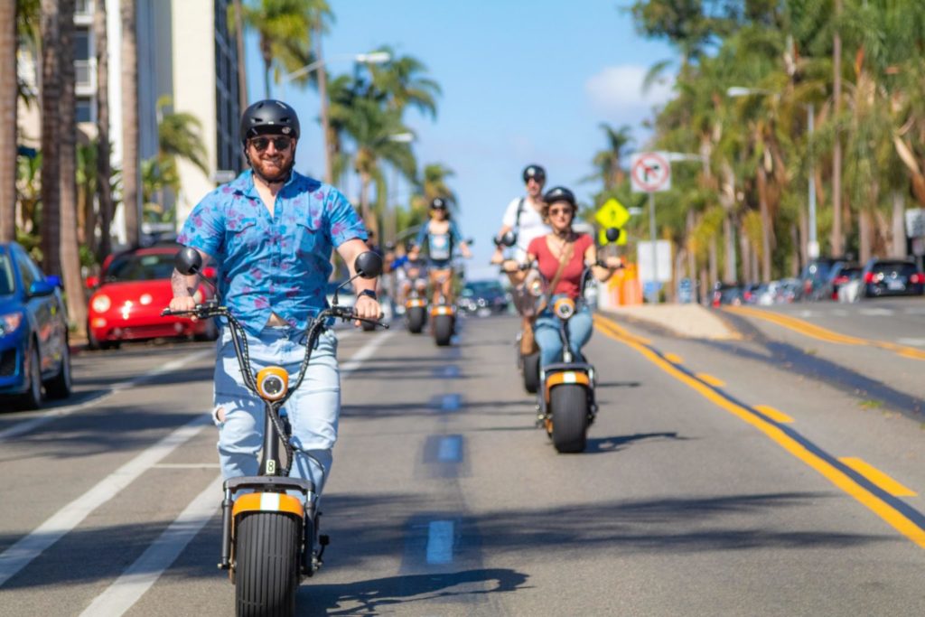 Several People Driving Fat Tire Scooters Near the Ocean in San Diego