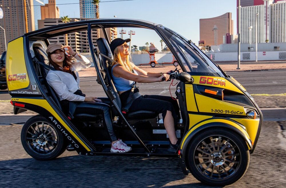 two women driving on a GoCar Las Vegas Tour with tall hotels in the background