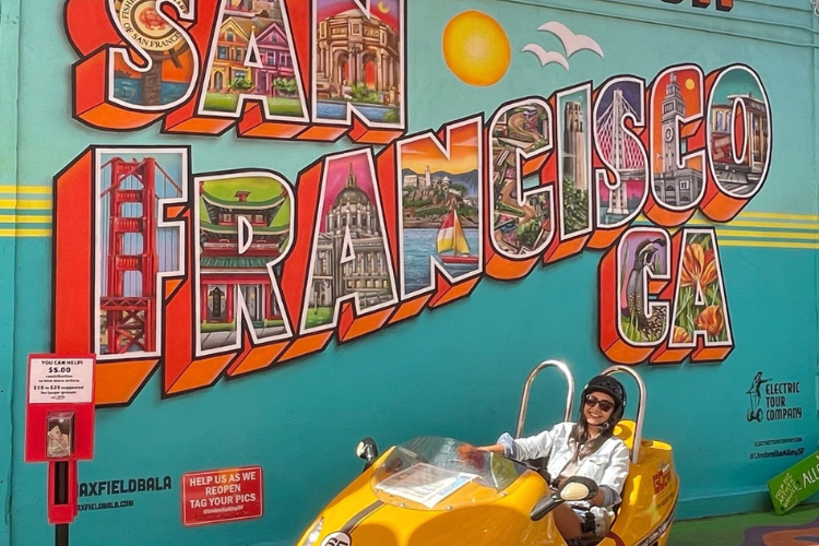 woman in GoCar parked in front of a colorful mural that reads San Francisco, CA