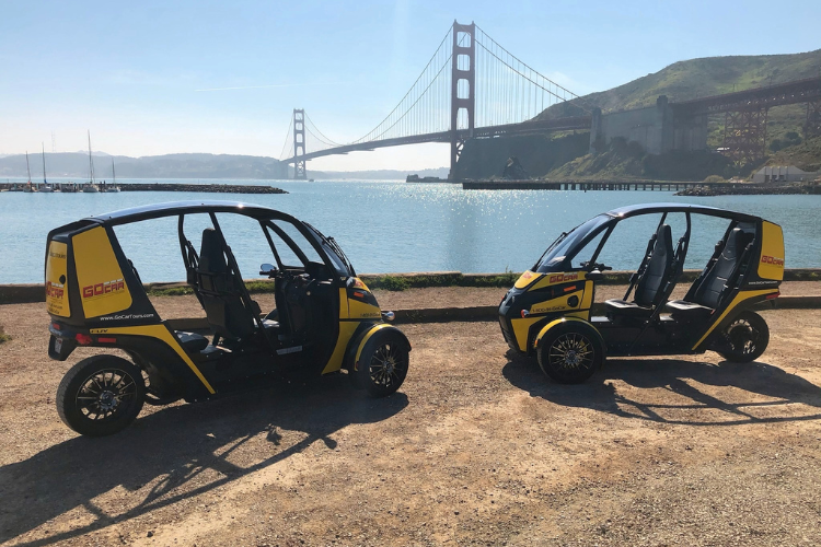 Two GoCars parked in the sun with the golden gate bridge in the background