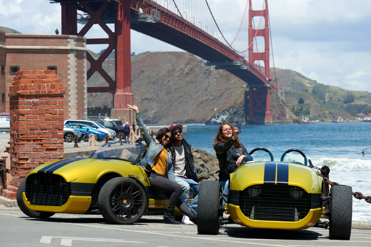 three people in GoCar V-Sports taking a selfie in front of the Golden Gate Bridge